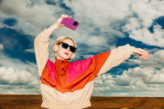Trendy blonde woman posing in retro sportswear listening to music outdoors