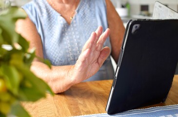 Modern grandma greets online, with tablet in hand. Online communication with family or friends.
