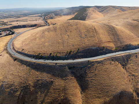 Aerial view of a high road winding around the side of a dry barren hill