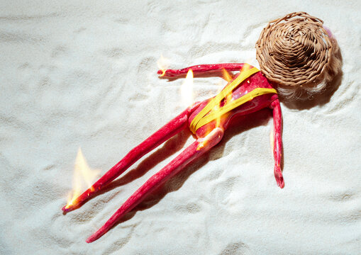 Doll with sunburn effect on beach sand as humorous skin cancer warning
