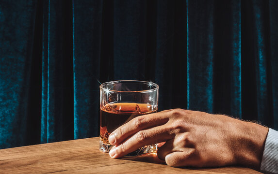 Hand holding whiskey glass on wooden bar table