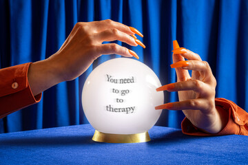 Hand with orange nails holding crystal ball with therapy message on blue velvet