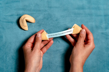 Hand holding fortune cookie with astrology message on blue velvet