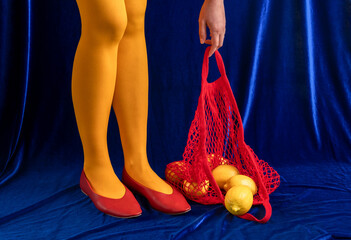 Woman in yellow tights with red shoes holding string bag of lemons