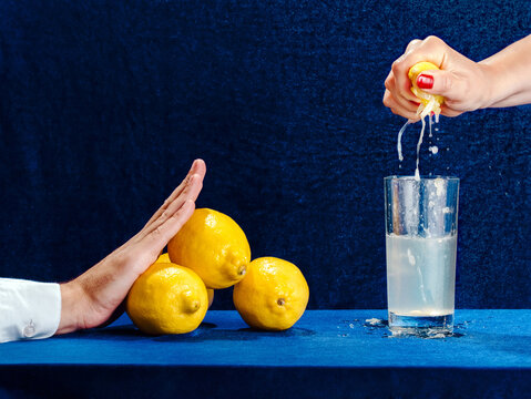 Woman squeezing lemon into glass as man gestures to refuse drink