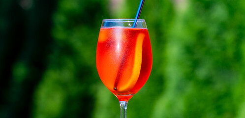 Aperol spritz cocktail in wine glass on a nature background. Classic italian aperitif aperol spritz cocktail with slice of orange. Closeup. Summer refreshing drink with sunlight