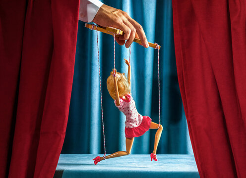 Hand controlling woman puppet on stage representing manipulation and humor