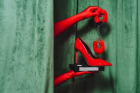 Red gloved hand holding high heel and handcuff with vintage cassette
