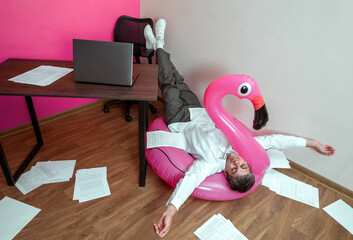 Overworked person lying on inflatable flamingo surrounded by office paperwork