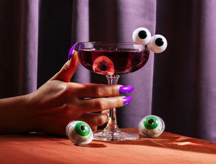 Hand with fake nails holding halloween cocktail with eyeball decor