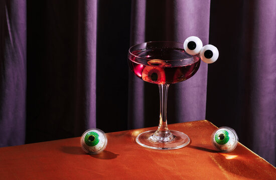Spooky Halloween cocktail with eyeball garnish on purple and orange background