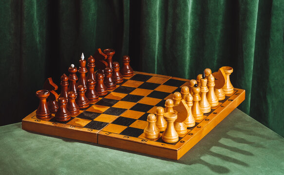 Wooden chessboard with pieces on green velvet table in retro still life