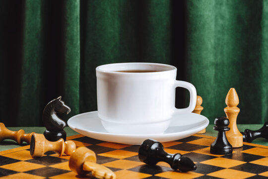 White coffee cup on chessboard with pieces and green velvet curtain