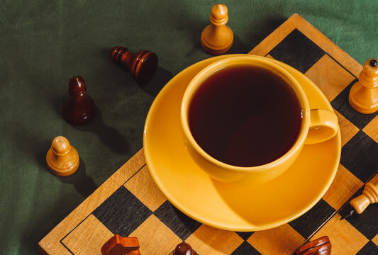 Yellow coffee cup on chessboard with game pieces and green velvet