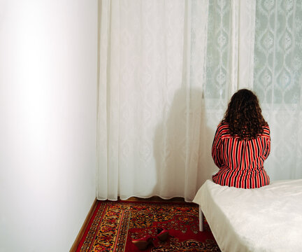 Person in striped outfit seated on bed facing curtain in retro room