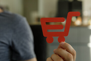 Close-up of a hand holding a red paper shopping cart icon.  Perfect for e-commerce, online...