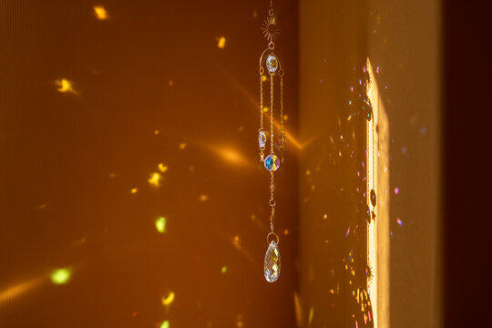 Glass suncatcher with metal golden chains, shining in sunlight and reflecting the rainbow on a yellow background