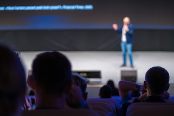 Blurred audience watching a speaker on stage delivering a dynamic presentation at a conference