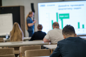 Blurred conference audience watching speaker presenting on a screen with displayed graphs.