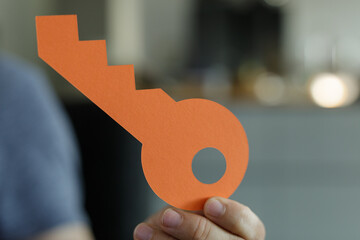 Image of a hand holding an orange paper key.  Represents success, opportunity, and growth. Perfect for business and motivational concepts.