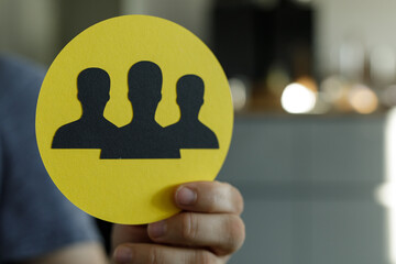 Image of a hand holding a yellow circle with three black silhouettes representing teamwork and...