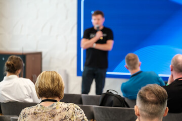 Obraz premium Speaker presenting in business seminar with audience in focus, highlighting learning and engagement atmosphere