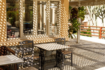 Stock photo of a sunny outdoor cafe patio with tables, chairs, and lattice shadows. Perfect for restaurant, cafe, or travel themes.