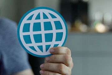 Close-up of a hand holding a teal paper cutout of a global network symbol.  Represents connection,...