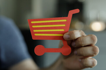 Close-up of a hand holding a red paper shopping cart icon.  Perfect for e-commerce, online...
