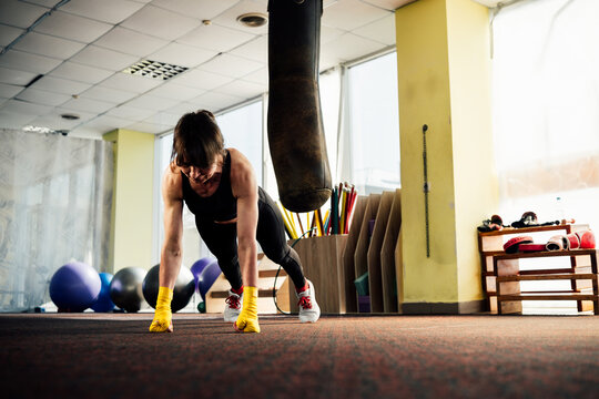 Female boxer doing push-ups in a gym with punching bag - Powered by Adobe