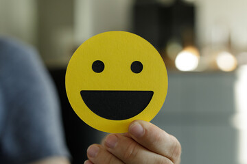 Person holding a yellow smiley face card.  Positive emotions, happiness, good mood.