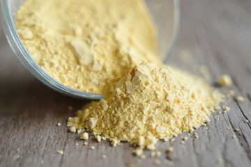 Fine yellow powder pouring out of a glass bowl onto a wooden surface
