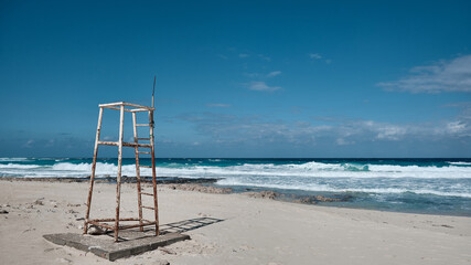 Rusty, weathered lifeguard tower stands alone on pristine sandy beach under vivid blue sky with...