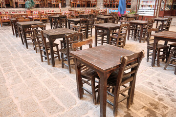 Rows of rustic wooden tables and chairs arranged in traditional courtyard cafe with stone-tiled...