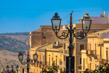 Decorative wrought iron street lamps with Mediterranean town buildings and hills in the background. © Christo