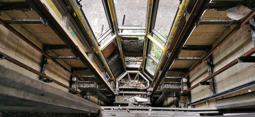 Collapsed elevator shaft ruins. Crashed fallen glass lift accident. Structural fire damage by arson. Towering inferno scene, burnt metal wreckage. Vertigo fear of heights, looking down over the edge. © MikeBeverley