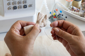A close-up shot shows a person's hands diligently sewing a small fabric craft item with a needle...