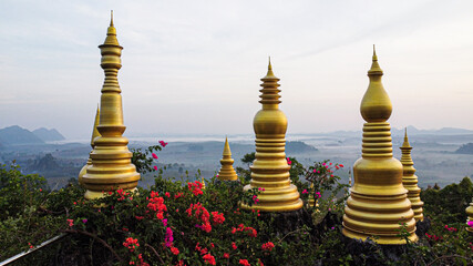 Fototapeta premium Golden pagodas at Khao Na Nai Luang Dharma Park, a famous Buddhist temple and spiritual landmark in Surat Thani, Thailand, with mountain view and colorful flowers at sunrise