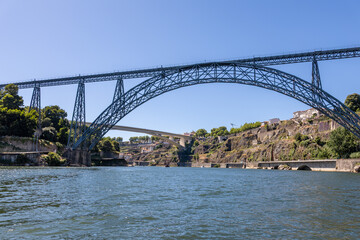 View from a boat on the Douro River, with a bridge framing the city of Vila Nova de Gaia under a clear sunny sky and calm river waters.