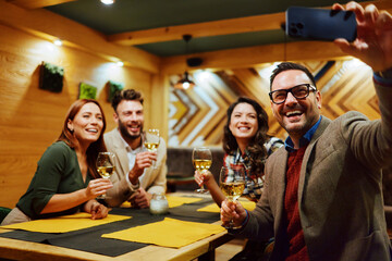 Happy friends taking selfie and drinking wine in restaurant