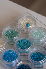 A vibrant collection of blue, green, and white seed beads neatly organized in clear containers. These colorful beads are perfect for jewelry making, embroidery, and other crafting projects.