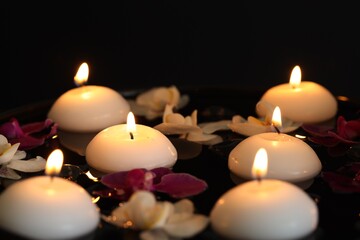 Burning candles and orchid flowers floating in water on black background, closeup