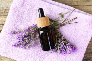 Lavender essential oil, flowers and towel on wooden table, top view