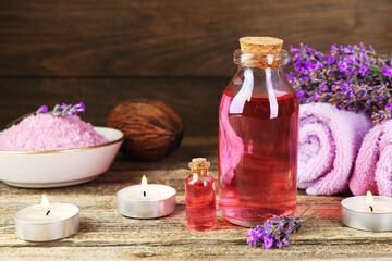 Lavender essential oil, flowers, candles, sea salt and towels on wooden table