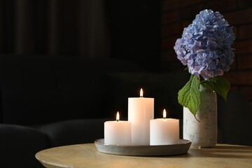 Burning candles and hydrangea flowers on wooden table at home. Space for text