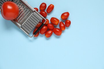 Fresh tomatoes and grater on light blue background, flat lay. Space for text