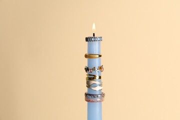 Burning candle with different rings on beige background