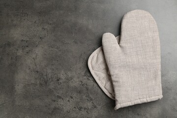 Grey oven glove and potholder on dark textured table, top view. Space for text
