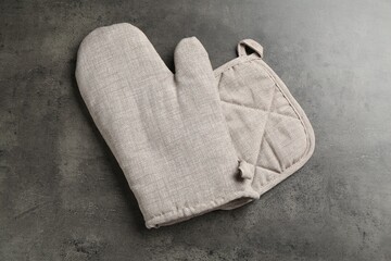 Grey oven glove and potholder on dark textured table, top view