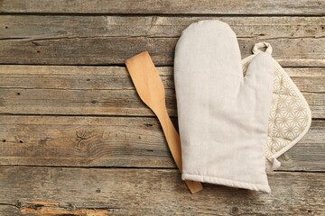 Oven glove, potholder and spatula on wooden table, flat lay. Space for text